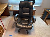 Front view of black leather padded office chair and clear floor protector mat beneath it.