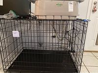 Front view of assembled black metal wire dog crate with plastic base tray inside and beige plastic pet feeder box on top.