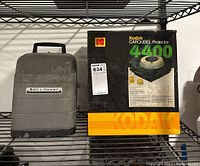 Kodak Carousel Projector 4400 box next to Bell & Howell carrying case on shelf.