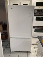 Front view of white Amana refrigerator with bottom freezer drawer showing entire appliance in kitchen setting.