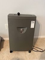 Front view of gray paper shredder with visible control knob on top and viewing window on front trash compartment.