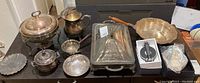 Photo showing multiple silver plated serving dishes and coasters arranged on a table, including trays, pitchers, plates, and a chafing dish.