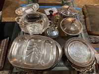 View of all silver plated servers including platters, bowls, butter dish with handle, tongs, and chalices arranged on a table.