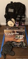 Overview of lot showing backpack, ear protection earmuffs, Cabela's cleaning kit box, four cans of gun oil, and black gun holster