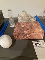 Wide view showing all four decor items: crystal cluster, polished stone box, quartz obelisk, and white banded stone on a surface with wall backdrop.