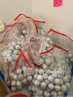 Photo showing multiple clear zip bags filled with used white golf balls with red-trimmed zipper backs.
