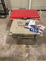 Tan Yeti cooler with owner's manuals and promotional materials on top. Red Igloo cooler behind.