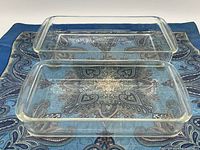 Photo of two clear rectangular Pyrex glass casserole dishes stacked next to each other on a blue patterned cloth.
