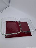 Two clear rectangular Pyrex baking dishes placed side by side on a maroon cloth background.