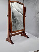 Full front view of the antique wooden framed vanity mirror with two carved feet and swivel stand.