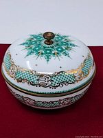 A closed view of the round Arta porcelain covered dish with intricate turquoise, black, and gold decoration, brass knob on lid.