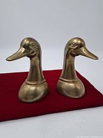 Pair of brass duck head bookends front view on red cloth background.