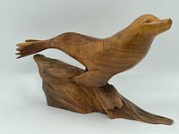 Side view of whole sculpture showing seal swimming with tail extended, mounted on wooden base that looks like driftwood.