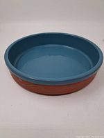 Side angle photo showing blue glazed interior and rim with terracotta exterior and decorative wave pattern.