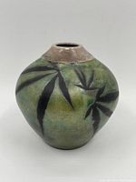 Front view of the ceramic vase showing green glaze with dark leaf patterns and natural finish rim.