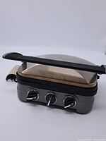 Side view showing the black handle, stainless steel floated lid, and control knobs at the front.