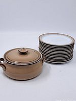 View of the ceramic pot next to the stack of 10 matching plates showing overall color and condition.