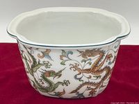 Side view of the porcelain bowl showing two colorful dragons and floral motifs on a white glaze background, scalloped rim with blue trim.