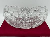 Crystal centerpiece bowl front view on red fabric backdrop showing detailed cut patterns and scalloped rim.