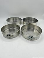 Four vintage metal springform cake pans with textured interiors and latch mechanisms, displayed side by side.