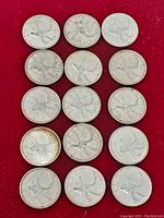 Fifteen Canadian silver quarters laid out on red background, all show the caribou reverse side.