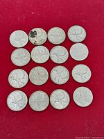 15 Canadian silver quarters laid out on red background showing caribou design on reverse side with varying years and wear.