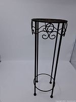 Full view of the tall vintage metal plant stand showing four legs and decorative top rim