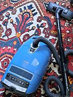 Full view of Miele Complete C3 canister vacuum on rug with attached hose and floor nozzle