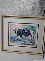 Front view showing original framed watercolour painting of a dairy cow with cream and gold frame, matting, and signature visible.