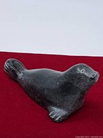 Soapstone seal figurine photographed from side view on red surface showing smooth curves and flipper details.
