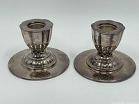 Pair of silver plate candle holders viewed from the front showing the rounded scalloped bases and tapered candle cups.