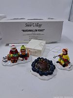Full view of Snow Village "Marshmallow Roast" box with three figurines and campfire base in front