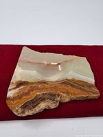 Full view of the rectangular stone ashtray placed on red fabric, showing polished surface with multicolor natural stone bands and carved concave bowl.