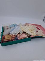 Overview photo showing open teal vintage Barbie carrying case with multiple folded vintage Barbie dresses and accessories inside.