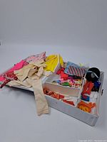 Open white vintage Barbie case showing assorted vintage Barbie doll clothes piled inside.