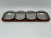 Front view of the metal dishes set on the wood tray, showing all four dishes and tray surface.