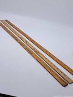 Three vintage wooden rulers laid out diagonally, showing full length and all measurement markings with advertising text visible