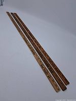 Three vintage wooden rulers laid on a plain surface showing their full length with printed advertising and measurement markings.