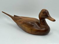 Side view of the wooden carved duck showing smooth surface and elongated tail.