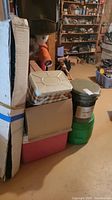 Side view of boxed hammock with green rope inside, metal cooler, and plastic coolers stacked