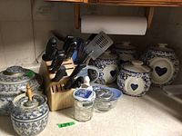 Wide shot of countertop showing ceramic canisters with blue heart, wooden knife block with knives, utensil jar with utensils, and small kitchen items.