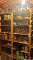Wide view of wooden shelves filled with assorted canning jars, boxes, and containers located in a basement with brick walls.
