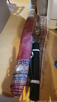 Rolled carpets showing a red patterned carpet with fringes and a plain black carpet mat, both secured with straps.