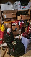 Stacked cardboard boxes and black garbage bags containing various Christmas decorations in basement storage.