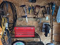 Overall view of clamps, extension cords, tool box, saw, grinder arranged against wall