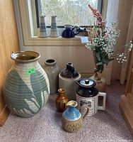 Full view of ten pottery items including crocks, jugs, vases and one syrup jug all arranged on carpet by window with natural light