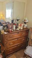 Photo showing wooden dresser with three drawers and various decorative items on top including a vintage kerosene lamp and figurines.