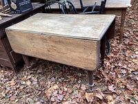Front and side view of antique wooden drop-leaf table with leaves down, showing weathered finish and turned legs.