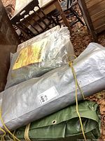 Lot showing three tarpaulins, two rolled and one in packaging.