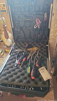 Open aluminum folding tool case containing assortment of hand tools laid on foam padding